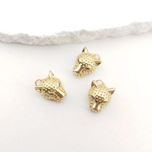 Puede incluir: Tres abalorios de metal dorado en forma de cabeza de leopardo. Cada abalorio tiene una superficie texturizada y un pequeño bucle para sujetarlo a un collar o pulsera.