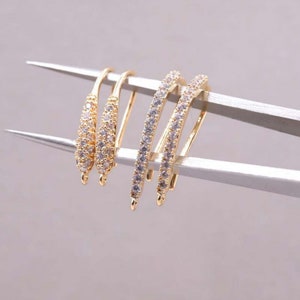 以下が含まれることがあります： 透明なキュービックジルコニアの石が付いた、金色のイヤリングフックが3つ。フックは湾曲しており、端に小さなループがあります。