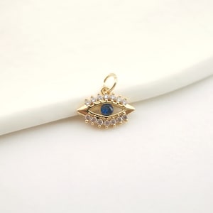 Op de afbeelding: Gouden boze oog bedel met blauwe en witte strass steentjes.