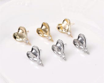 May include: Six heart-shaped stud earrings. Three are gold-toned, and three are silver-toned. Each earring has a small, clear gemstone accent at the bottom. The earrings are displayed on a white surface.