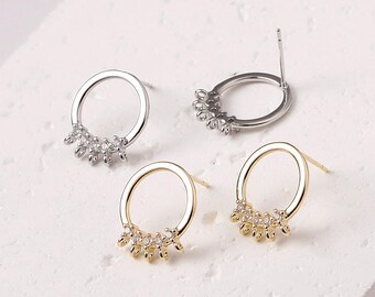 May include: Four pairs of earrings. Two pairs are silver-toned, and two are gold-toned. Each earring features a circular design with a cluster of small, clear stones at the bottom. The earrings are displayed on a white surface.