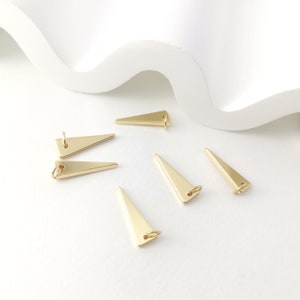 May include: Five gold triangle-shaped charms with a loop at the top. The charms are arranged on a white surface.