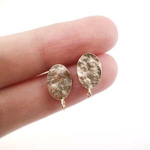 May include: A pair of gold oval-shaped earring blanks with a hammered texture and a jump ring attached to the bottom.