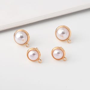 May include: Four gold-colored stud earrings with a round, off-white pearl center. Each earring has a small loop at the bottom. The earrings are set against a white background.