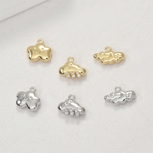 Puede incluir: Una colección de colgantes de nube y estrella dorados y plateados. Los colgantes tienen un lazo en la parte superior para colgar y presentan caras sonrientes. Algunos colgantes de nube tienen tres pequeñas piedras transparentes.