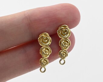 Könnte beinhalten: Goldfarbene Ohrringe mit einem kaskadierenden Rosen-Design. Jeder Ohrring hat drei rosenförmige Elemente, die vertikal angeordnet sind. Die Ohrringe haben unten eine kleine Schlaufe zur Befestigung. Der Hintergrund ist hell und neutral.