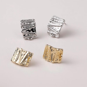 May include: Four square-shaped stud earrings. Two are silver-colored, and two are gold-colored. Each earring has a textured, folded design. The earrings are displayed on a light background.