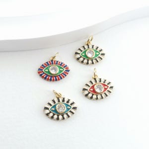 May include: Four gold-coloured eye-shaped charms with colourful enamel details. Each charm features a central clear stone and is surrounded by a design in red, blue, green, and black. The charms are designed for jewellery making.