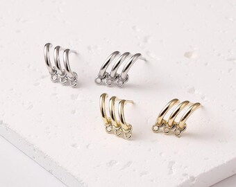May include: Four pairs of earrings in silver and gold tones are displayed on a white surface. Each earring features three curved hoops connected at the bottom with small rings. The earrings are designed for pierced ears.