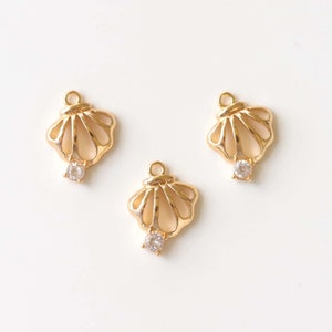 Könnte beinhalten: Drei goldfarbene Metall-Anhänger in Form von Muscheln mit einem klaren Strassstein in der Mitte jedes.