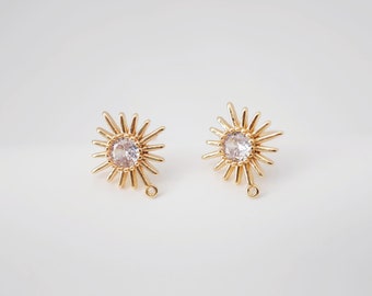 May include: A pair of gold earrings with a starburst design and a clear crystal in the centre. Each earring has a small loop hanging from the bottom.