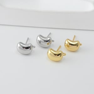 May include: Four pairs of bean-shaped stud earrings. Two pairs are silver-colored, and two pairs are gold-colored. Each earring has a post for piercing and a small loop at the bottom. The earrings are on a white surface.