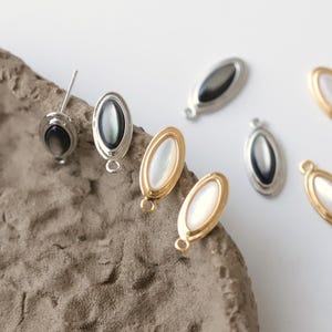 Pu&ograve; includere: Primo piano di vari componenti di gioielleria di forma ovale. Alcuni sono argentati con un centro scuro e iridescente, mentre altri sono dorati con un centro bianco perlaceo. I componenti hanno piccoli anelli per il fissaggio, suggerendo orecchini o pendenti.