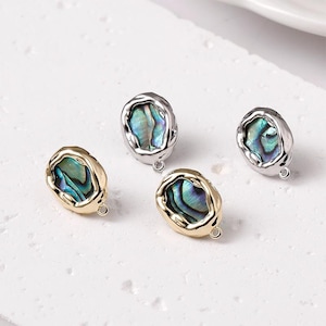 May include: Four oval-shaped jewelry components. Two are gold-toned, and two are silver-toned. Each features a vibrant, iridescent abalone shell inlay with shades of blue, green, and purple. Small loops are attached for jewelry making.