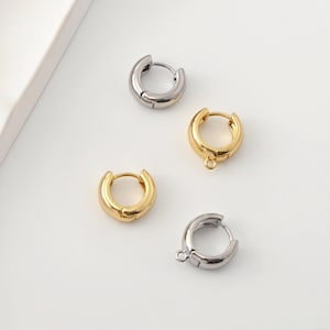 Può includere: Quattro piccoli orecchini a cerchio in tonalità oro e argento sono esposti su una superficie bianca. Due sono dorati e due argentati. Gli orecchini hanno un design semplice e arrotondato, con una chiusura a cerniera.