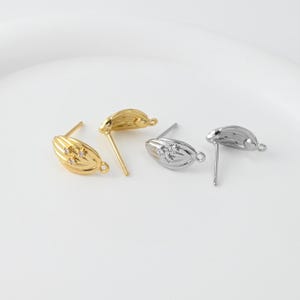 May include: Gold and silver-toned stud earrings. The gold earrings have a textured, oval design with three small, clear stones. The silver earrings have a similar shape with a cluster of clear stones. Both have a post and loop for attachment.