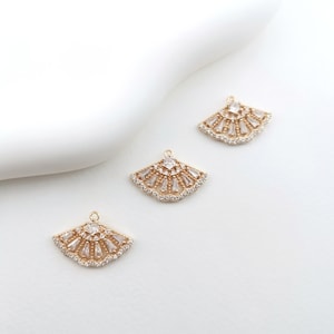 Könnte beinhalten: Drei goldfarbene Fächer-Anhänger mit klaren Kristallverzierungen. Die Anhänger haben ein zartes, filigranes Design und wären perfekt, um Schmuckprojekten einen Hauch von Glanz zu verleihen.