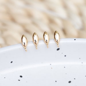 May include: Four gold-colored leaf-shaped jewelry findings with a loop at the bottom.