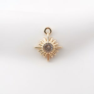 Può includere: Ciondolo a forma di stella dorata con un strass trasparente al centro. Il ciondolo ha un anello in alto per essere attaccato a una collana o un braccialetto.