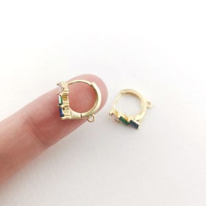 May include: Gold hoop earrings with a small row of colorful stones. The stones are pink, green, and blue.