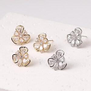 May include: Five flower-shaped stud earrings. Two pairs are gold-toned, and one pair is silver-toned. Each earring features clear, sparkling crystals arranged in a floral pattern. The earrings have a post and loop for attaching to other jewelry.