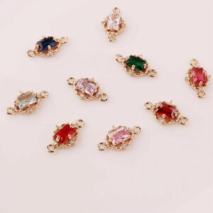 May include: Assortment of gold-tone connector charms with colourful gemstone accents. Each charm features a rectangular gemstone surrounded by smaller clear stones and two loops for attaching to jewellery.