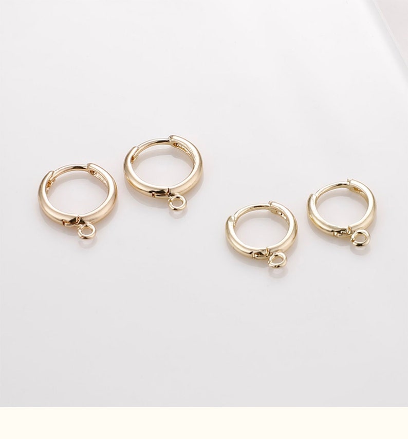 May include: Four gold hoop earrings with a small jump ring attached to the bottom of each hoop.