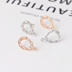 May include: Four teardrop-shaped earrings in gold, silver, and rose gold. Each earring features a series of small, rectangular, clear crystals. The earrings have a small loop at the bottom for attachment. The background is white.