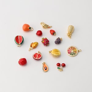 May include: A collection of colorful fruit charms, including a watermelon slice, cherries, and a pineapple. Each charm has gold-colored metal accents. The charms are in various shapes and sizes, with bright colors and detailed designs.
