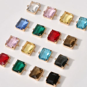 Könnte beinhalten: Sortiment aus bunten rechteckigen Glasperlen mit goldenen Metallverbindungsschlaufen. Die Perlen sind in verschiedenen Farben, darunter rosa, blau, grün, gelb, rot, braun, schwarz und klar.