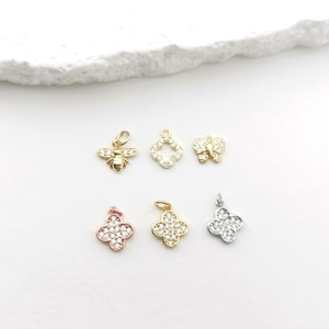 May include: Assortment of gold, silver, and rose gold charms with clear crystal accents. The charms include a bee, a four-leaf clover, a butterfly, and a square.