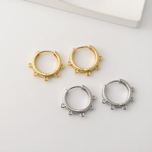 May include: Four hoop earrings, two gold and two silver. The gold earrings have a polished finish, the silver ones a matte finish. Each earring features multiple small loops for attaching charms. The earrings are displayed on a white surface.