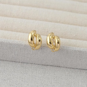 以下が含まれることがあります： 金色のイヤリングのペア。各イヤリングは、下部に小さなループが付いたユニークな、絡み合ったデザインを特徴としています。イヤリングは、明るい色のテクスチャのある表面に表示されています。