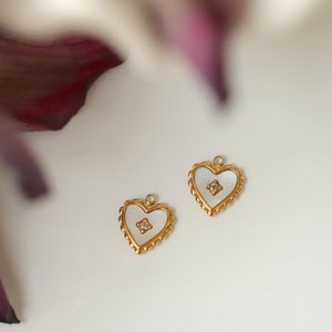 May include: Two gold heart-shaped pendants with a white mother-of-pearl inlay and a small clear rhinestone in the centre.