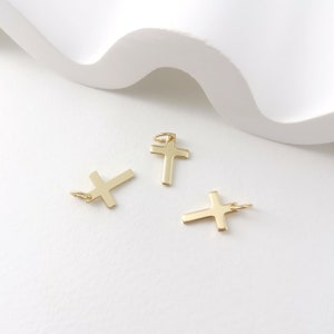 Op de afbeelding: Drie gouden kruisbedels met een lus aan de bovenkant om aan een ketting of armband te bevestigen.