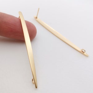 Puede incluir: Un par de cierres de pendientes de color dorado con una forma larga, delgada y cónica. Cada cierre tiene un pequeño bucle en la parte inferior y un poste en la parte superior.