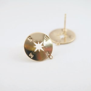 May include: Gold compass earrings with a star cut-out in the centre. The earrings are marked with the directions N, S, E, and W.