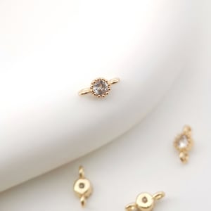 May include: Gold-toned metal connector with a clear rhinestone in the centre. The connector has two loops on either side.