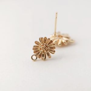 May include: Gold-toned flower shaped earring with a small loop hanging from the bottom. The earring is designed to be a dangle style.