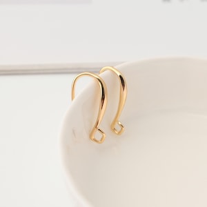 Peut inclure: Une paire de crochets de boucle d'oreille en métal doré au design lisse et incurvé. Chaque crochet présente une finition polie et une petite boucle en forme de losange à la base pour attacher des éléments de bijouterie, offrant une fixation sûre.