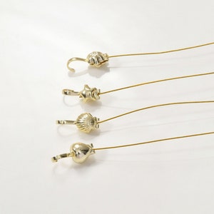 May include: Four gold-coloured metal charms with different shapes, including a seashell, a star, a heart, and a scallop shell. Each charm is attached to a thin gold wire.