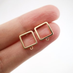 Könnte beinhalten: Zwei goldene quadratische Ohrringrohlinge mit einem Sprungring, der an der Unterseite jedes Rohlings befestigt ist.