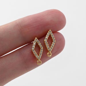 Pode incluir: Dois pingentes de joalheria dourados em forma de losango. Cada pingente é delineado com pequenos cristais transparentes. Uma pequena argola é presa à parte inferior de cada losango. Os pingentes são exibidos em um fundo claro.
