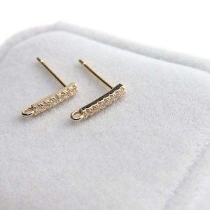 May include: A pair of gold-tone earring posts with a small, clear crystal bar. The bar is set with small, clear crystals.