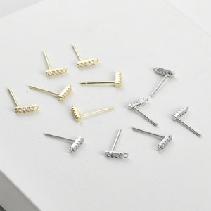 Könnte beinhalten: Ein Set aus zehn goldenen und silbernen Ohrsteckern mit kleinen, klaren Zirkonia-Steinen. Die Ohrringe haben die Form einer kurzen Stange mit abgerundeten Enden.