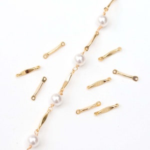 Puede incluir: Un collar de cadena de oro con cuentas de perlas blancas y conectores de barra de oro. El collar está colocado sobre una superficie blanca con conectores de barra de oro adicionales esparcidos alrededor.