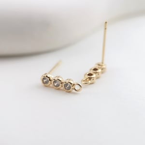 May include: Gold earring with three clear stones and a loop at the end.