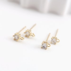 May include: Three gold-toned earring posts with clear round rhinestones and a small loop at the top.