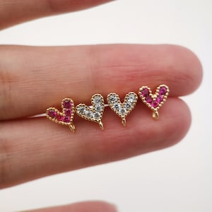 May include: Four gold heart-shaped charms with clear and pink cubic zirconia stones. The charms have a loop at the top for attaching to jewelry.