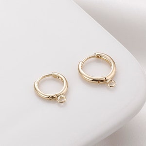 May include: Two gold hoop earrings with a small loop hanging from the bottom of each hoop.